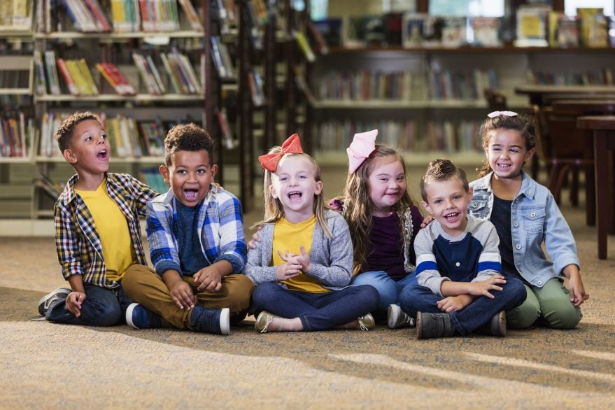 Group of diverse children sitting together in a library smiling and laughing